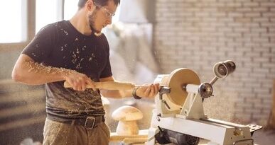 man using a white jet lathe to shape a wooden bowl in a workshop