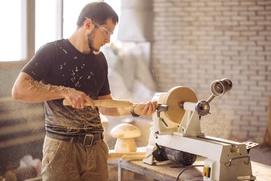 man using a white jet lathe to shape a wooden bowl in a workshop