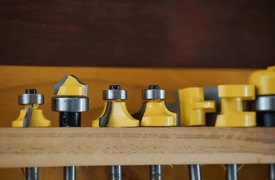 a row of yellow router bits with silver ball-bearing pilots organized in a wooden rack.