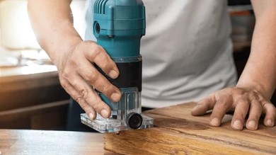 man using a palm router to cut the edge of a wooden board on a workbench