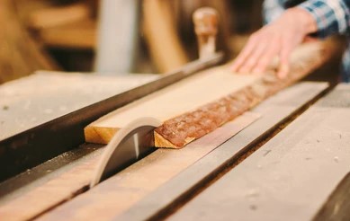worker cutting a hardwood board on a table saw with a rip fence