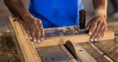hands guiding a wooden board through a table saw