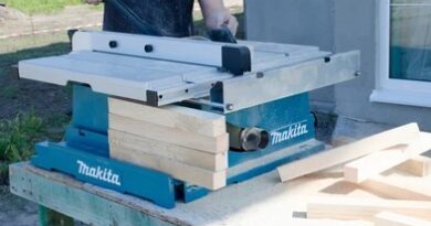 a person uses a push stick to feed a piece of wood through a blue Makita table saw on an outdoor workbench.
