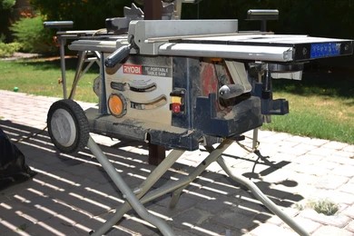 A ryobi 10-inch portable table saw with a folding wheeled stand set up on an outdoor patio